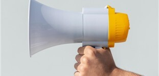 weiß-gelbes Megafon auf grauem Hintergrund, gehalten von einer Hand